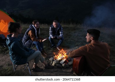 Group Of Friends Gathering Around Bonfire At Camping Site In Evening