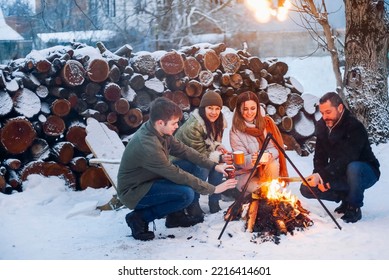 Group of friends gathering around bonfire in backyard, drinking tea and warming hands. Two happy couples relaxing and enjoying winter season while sitting around fire. Outdoor winter entertaining - Shutterstock ID 2216414601