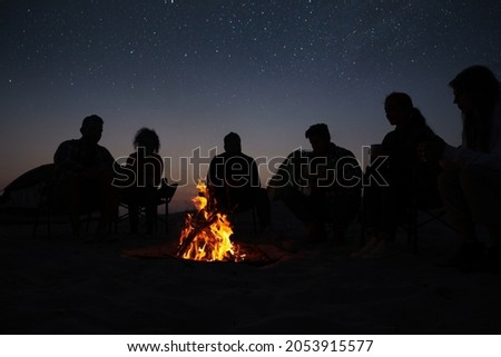 Group of friends gathering around bonfire in evening. Camping season