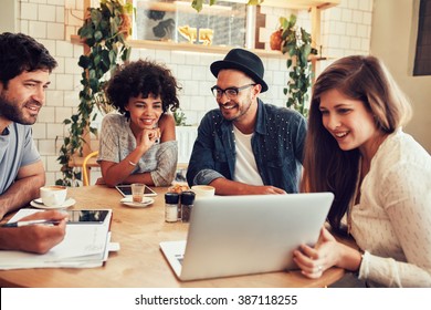 Group Of Friends Hanging Out In A Coffee Shop With A Laptop Amongst Them. Happy Young People Sitting At Restaurant Using Laptop Computer.