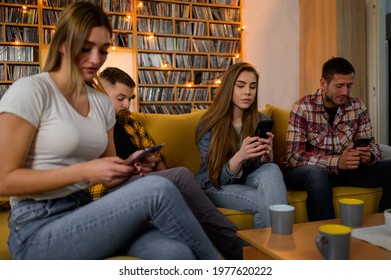 A group of friends hanging out on a house party while using smartphones and ignoring each other - Powered by Shutterstock