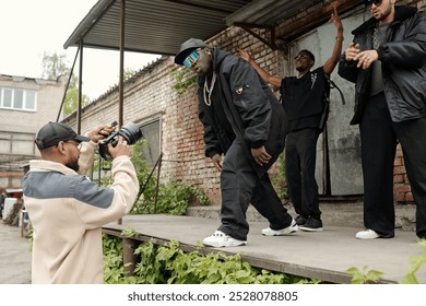 Group of friends hanging out outdoors, posing for camera while photographer captures moment. Industrial backdrop with concrete and greenery adds urban vibe - Powered by Shutterstock