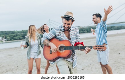 Group Of Friends Hangout At The City Beach.One Guy Plays Guitar And Singing While His Friends Dancing Around Him.	
