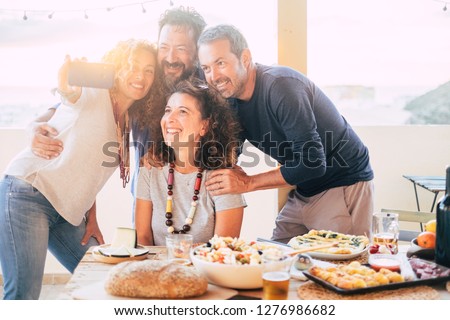 Group of friends have fun together during a lunch outdoor in the terrace at home and taking a modern selfie with smart phone to share on social media accounts for internet life - web addicted happy