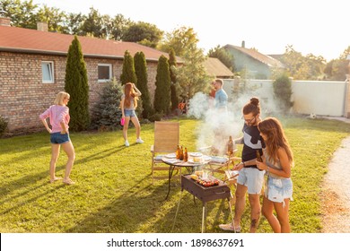 Group Of Friends Having A Backyard Barbecue Party, Grilling Meat, Drinking Beer, Playing Frisbee And Having Fun On A Sunny Summer Day