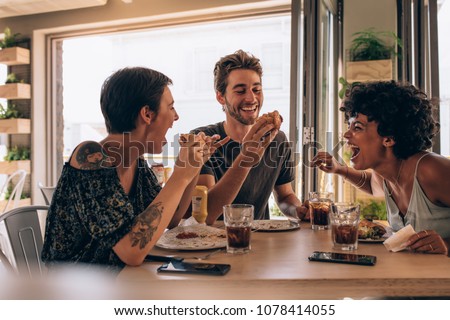 Group of friends having burger at restaurant. Cheerful young people eating burger and enjoying at a fast food restaurant.