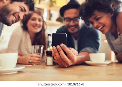 Group Of Friends Having Fun At The Cafe And Looking At Smart Phone. Man Showing Something To His Friends Sitting By, Focus On Mobile Phone.