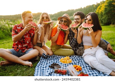 Group of friends having fun eating watermelon on the picnic outdoors. Foods, travel, nature and vacations concept - Powered by Shutterstock