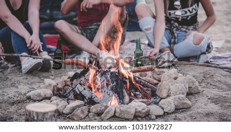 Group of friends having fun making BBQ on bonfire and relaxing by a lake. 