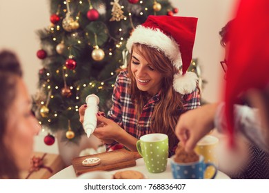 Group of friends having fun on Christmas morning, decorating Christmas cookies and drinking coffee - Powered by Shutterstock