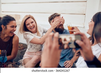 Group of friends having fun at a party with man taking a photo on a smart phone. Young people enjoying a party together. - Powered by Shutterstock