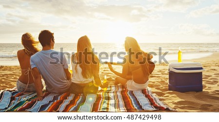 Group of friends having fun relaxing on the beach at sunset