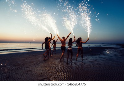 Group of friends having fun running on the beach with sparklers - Powered by Shutterstock