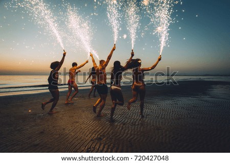 Group of friends having fun running on the beach with sparklers