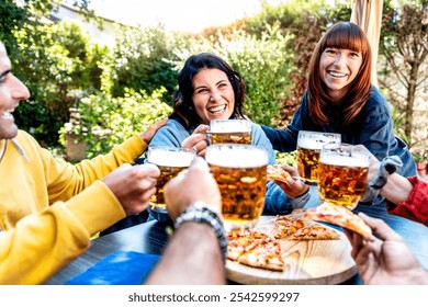 Group of friends having fun together toasting with beer mugs on a rustic table loaded with pizza in a beer garden - Young smiling people having fun toasting to the party in the restaurant bar - Powered by Shutterstock