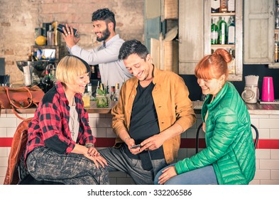 Group Of Friends Having Fun Using Smartphone At Hipster Cocktail Bar Restaurant - Young Man With Two Happy Young Women And Barman - Lifestyle Concept With People Relaxing And Socialising After Work