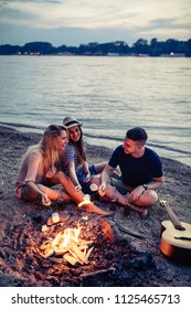 Group Of Friends Having Fun While Roasting Marshmallows Over A Fire On The Beach