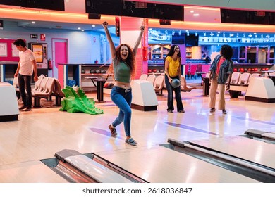 Group of friends having fun while playing bowling, one of them is celebrating a strike with arms raised