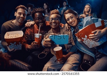 Group of friends having fun while taking selfie during movie projection in a theater. 