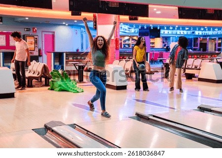 Group of friends having fun while playing bowling, one of them is celebrating a strike with arms raised