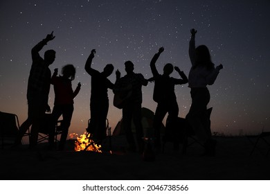 Group of friends having party near bonfire in evening. Camping season