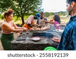 Group friends having party outdoors, focus on barbecue grill with food – multigeneration family grilling outside on backyard in garden party – group of multiracial diverse people having fun barbecuing