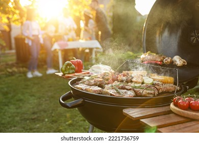 Group of friends having party outdoors. Focus on barbecue grill with food. Space for text - Shutterstock ID 2221736759