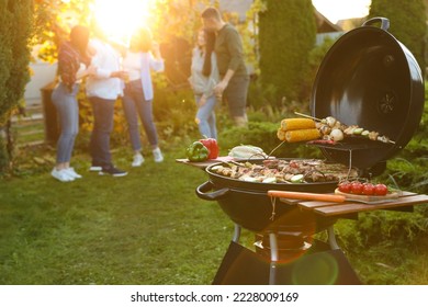 Group of friends having party outdoors. Focus on barbecue grill with food. Space for text - Shutterstock ID 2228009169
