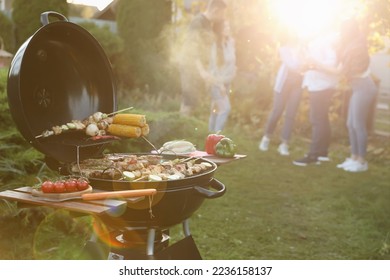 Group of friends having party outdoors. Focus on barbecue grill with food. Space for text - Shutterstock ID 2236158137