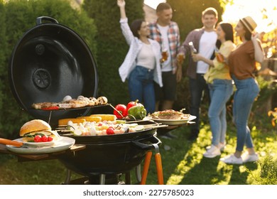 Group of friends having party outdoors. Focus on barbecue grill with food - Powered by Shutterstock