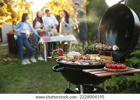 Group of friends having party outdoors. Focus on barbecue grill with food. Space for text
