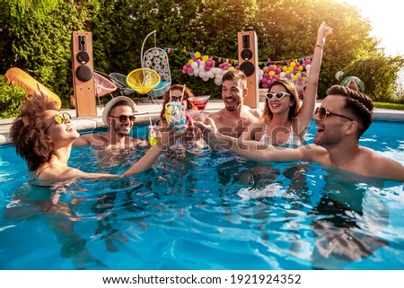Group of friends having party in pool, drinking cocktails and enjoying together.