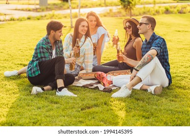 Group of friends having a picnic in the park on a sunny day, drinking beer drinks and eating pizza sitting on the grass on a sunny summer day, People hanging out, having fun while relaxing - Powered by Shutterstock