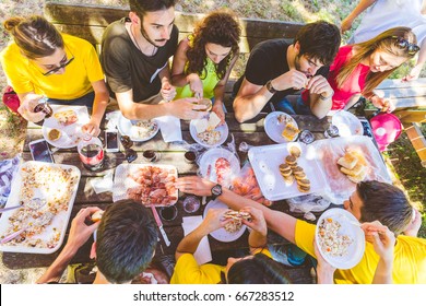 Group Of Friends Having Picnic At Park. Large Multiracial Group Of People Sitting At A Table And Eating Together On A Summer Day. Friendship, Vacations And Lifestyle Concetps