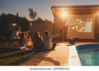 Group of friends having a surprise birthday party in an open air cinema, watching a movie by the swimming pool and waving with sparklers - Powered by Shutterstock