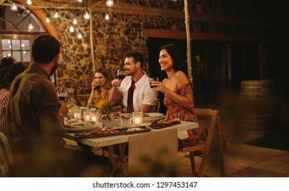 Group Of Friends Having Wine At Dinner Party. Young People Got Together By Table With Food And Drinks To Celebrate A Special Occasion.