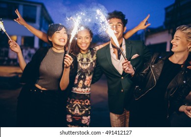 Group Of Friends Holding Sparklers Out On Street At Night. Young Men And Women Having Night Party With Sparklers.