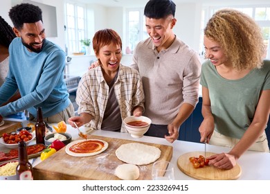 Group Of Friends At Home In Kitchen Adding Sauce To Homemade Pizzas For Party Together - Powered by Shutterstock