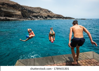 Group Of Friends Jumping Off Together At The Beach Doing Flips And Having Fun In The Water - People Enjoyinng Thei Holiday At The Beach Playing And Laughing