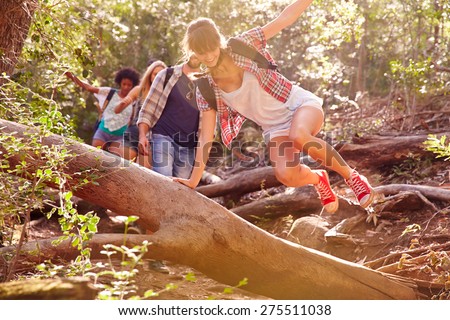 Group Of Friends Jumping Over Tree Trunk On Countryside Walk