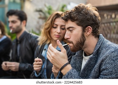 Group of friends lighting cigarettes and smoking together sitting on a bench outdoors - bad habits and addiction people lifestyle concept - Powered by Shutterstock