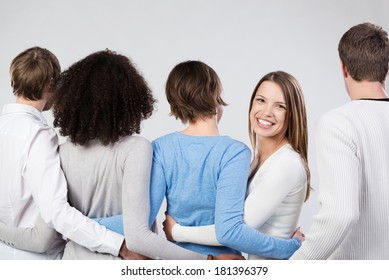 Group Of Friends Linking Arms Facing Away From The Camera With An Attractive Young Woman Turning To Look Back With A Beautiful Friendly Smile