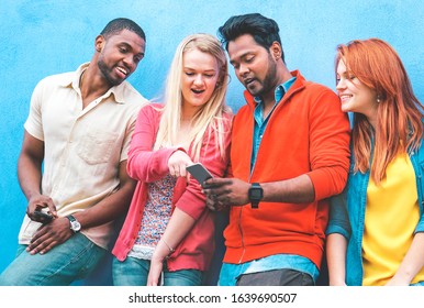 Group Of Friends Looking At Phone Pointing Finger In Surprised Faces On Blue Background - Multiracial Teenagers Using Smartphone In Happy Attitude - Lifestyle Concept Of  Generation X Trends - Image