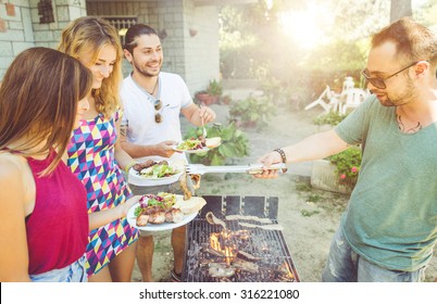 Group Of Friends Making Barbecue In The Garden Backyard. Friends Sharing Food And Happy Moments