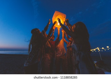 Group of friends making party on the beach at sunset time
