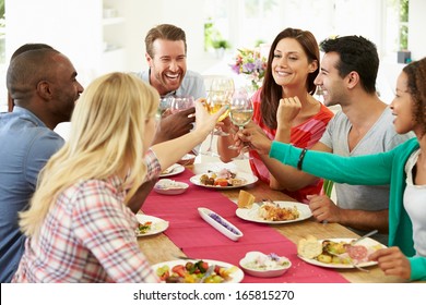 Group Of Friends Making Toast Around Table At Dinner Party