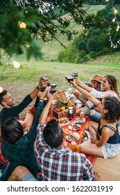 Group Of Friends Making A Toast During A Barbecue In The Countryside Under A Tree - Happy People Having Fun At A Picnic On The Hills In Summer