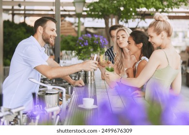 Group of friends, men and women enjoys refreshing cocktails in relaxed outdoor setting, modern bar, drinking with bartender. Concept of friendship, party, leisure, celebration, relaxation - Powered by Shutterstock