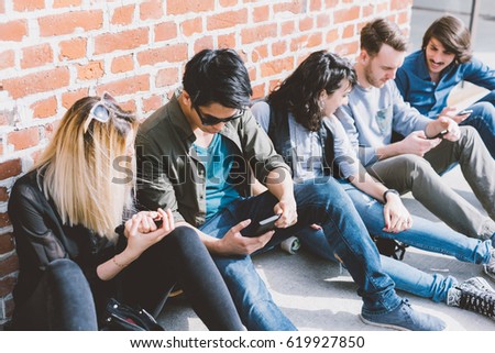 Group of friends multiethnic millennials sitting outdoor using smart phone - technology, having fun, togetherness concept