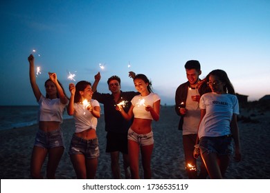 Group Of Friends At Night On The Beach With Sparklers. Young Friends Enjoying On Beach Holiday. Summer Holidays, Vacation, Relax And Lifestyle Concept.